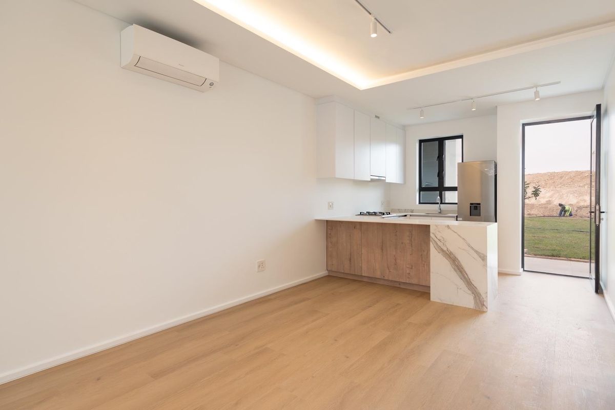 Modern open-plan kitchen and living area featuring light wood-look flooring, sleek cabinetry, stone-topped island, and integrated air conditioning, leading to an outdoor space.