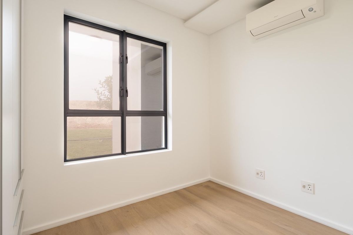 A bright, modern, and empty bedroom featuring light laminate flooring, a built-in wardrobe, and a wall-mounted split-system air conditioner.