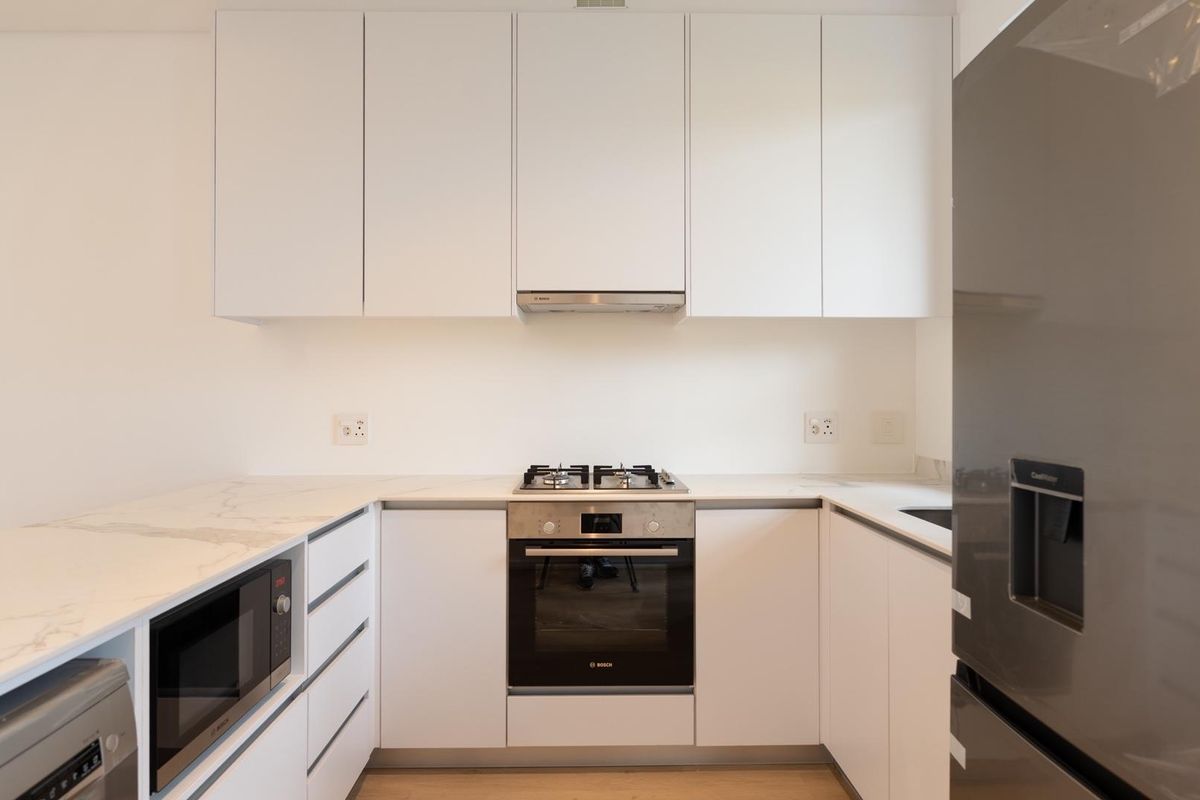 Modern kitchen featuring sleek white cabinetry, marble-look countertops, and integrated stainless steel appliances including a gas hob, oven, and microwave.