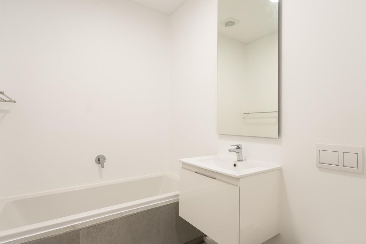 A clean, modern bathroom featuring a wall-mounted vanity with integrated basin, a bathtub, and a large wall-mounted mirror.