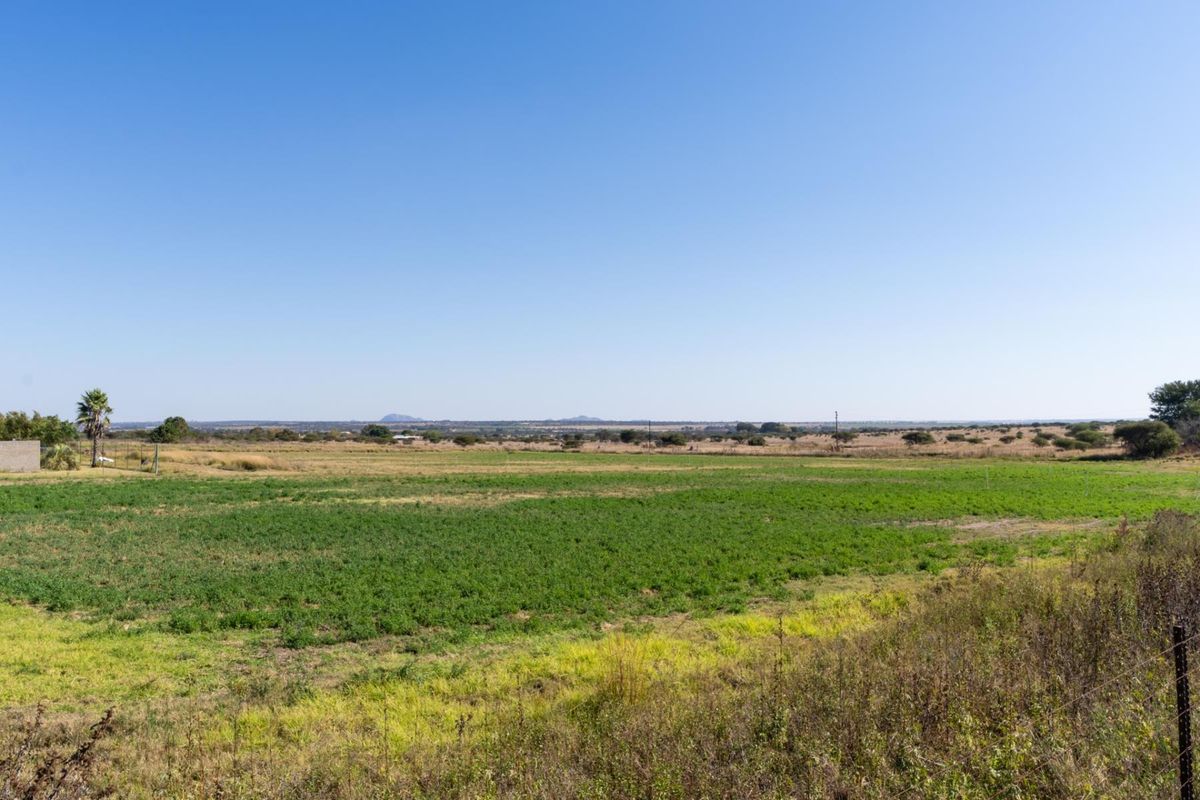 A wide-angle view of a large, open residential vacant land plot with natural vegetation and distant landscape views.