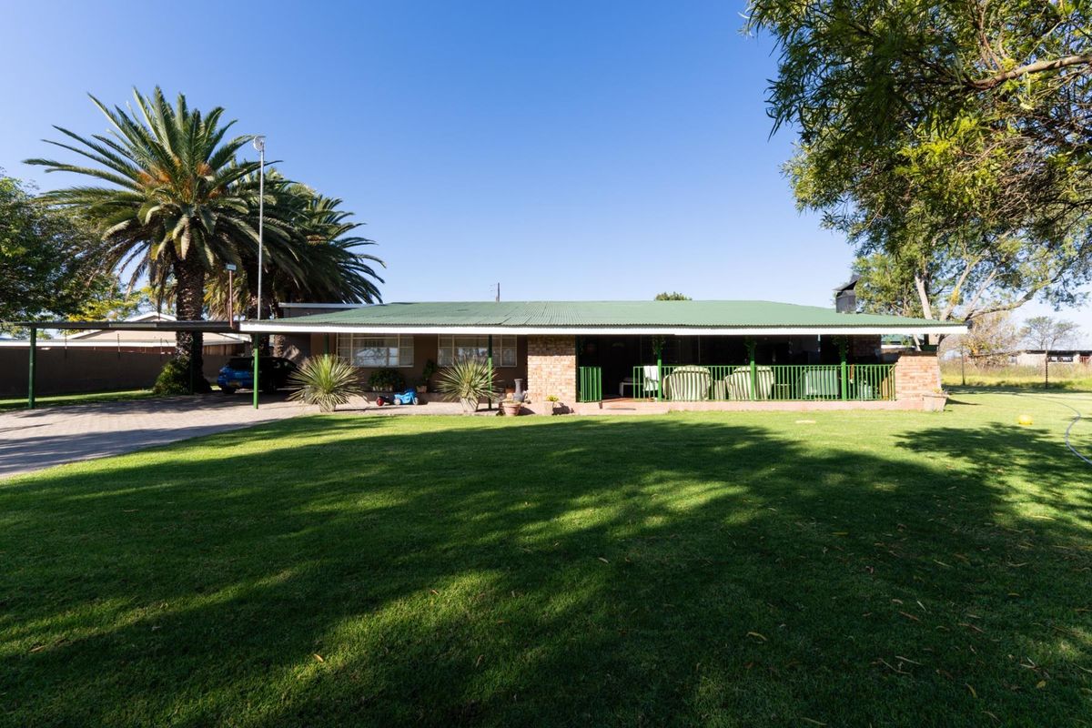 Rear view of a single-story residential property featuring a covered patio, brick exterior, metal roofing, and a spacious landscaped lawn.