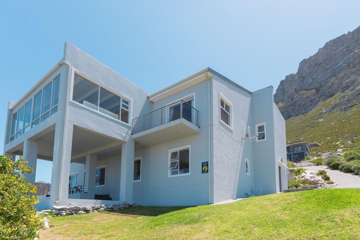 Rear view of a modern multi-level house featuring a balcony, large windows, and a scenic mountain backdrop.