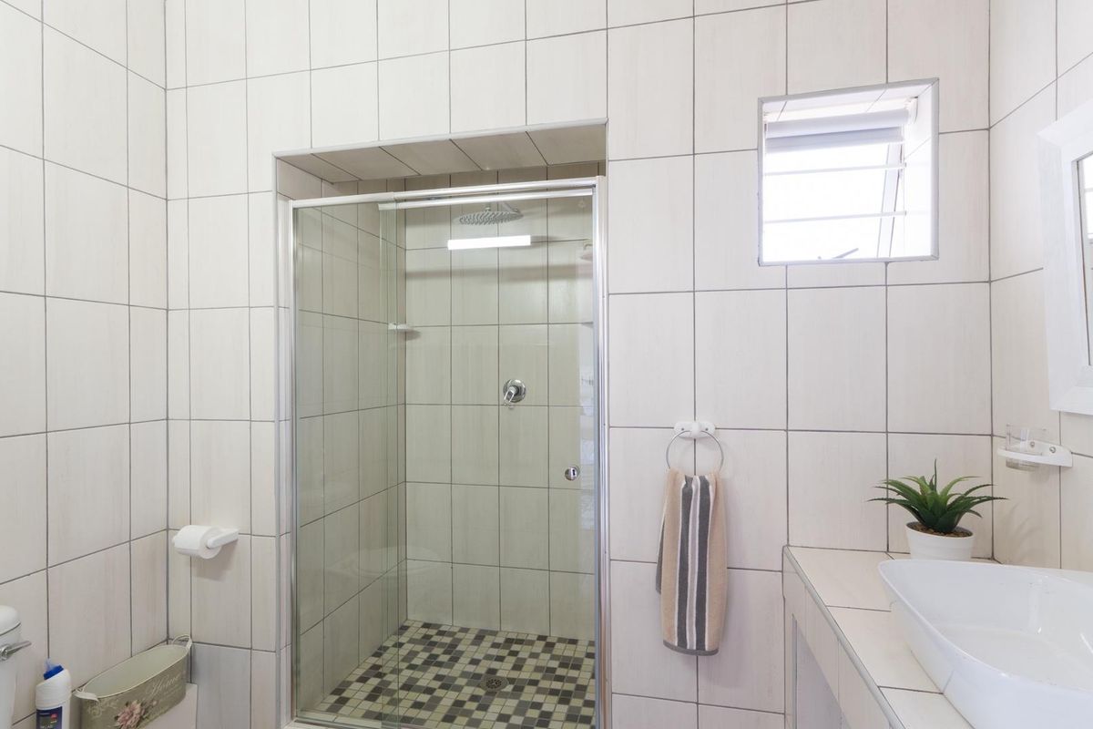 A clean, modern bathroom featuring a glass-enclosed shower with a rain shower head, tiled walls, and a contemporary vanity basin.
