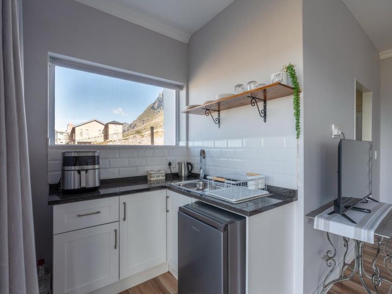 A compact and functional scullery area featuring white shaker cabinetry, granite countertops, a subway tile backsplash, and a stainless steel sink.