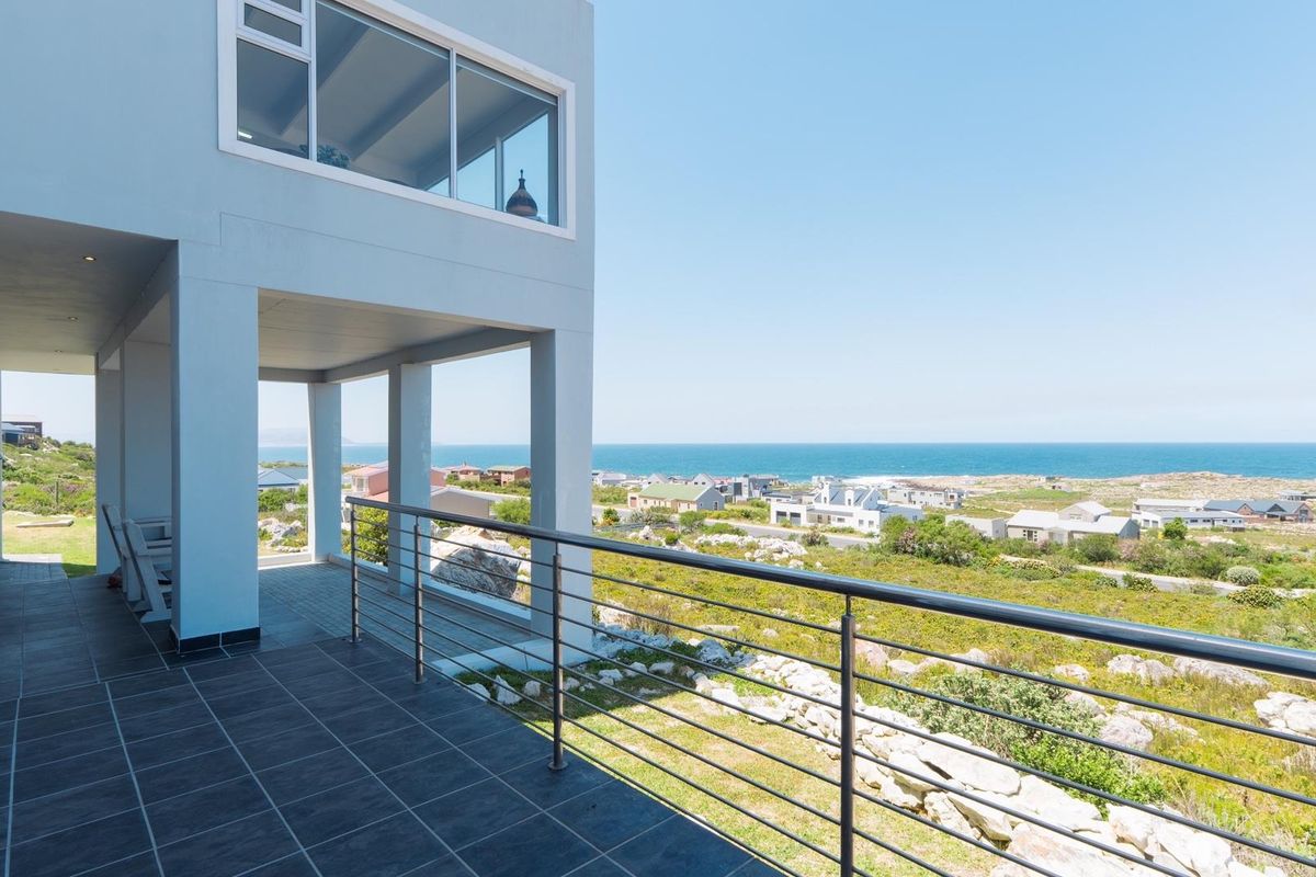 A spacious covered balcony featuring modern tiled flooring and a stainless steel balustrade, offering expansive coastal and neighbourhood views.