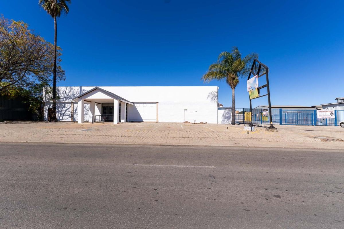 Front exterior view of an industrial property featuring a paved driveway, covered entrance, and perimeter security fencing.