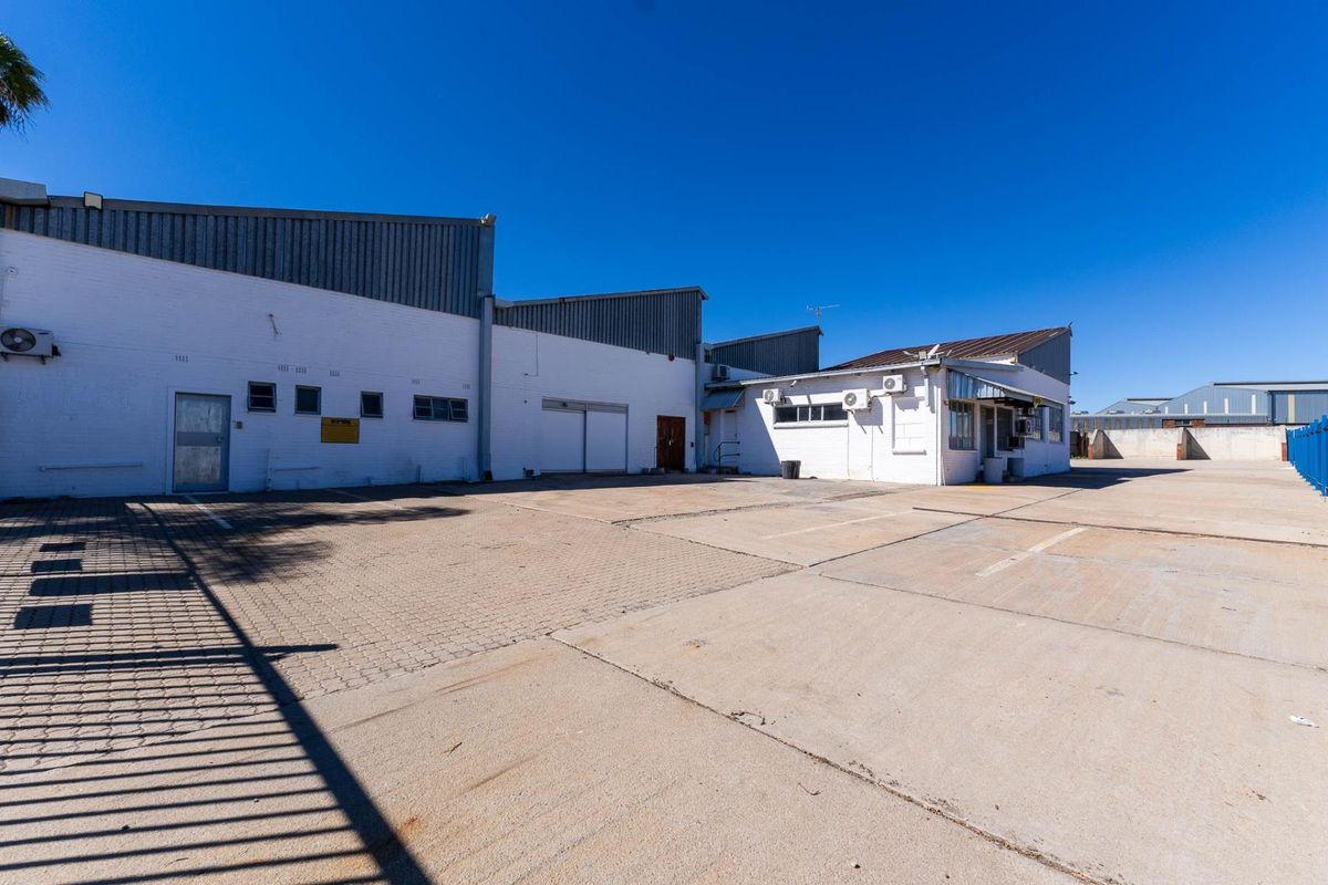 Rear exterior view of an industrial property featuring a large concrete yard, brick facade, and multiple air conditioning units.