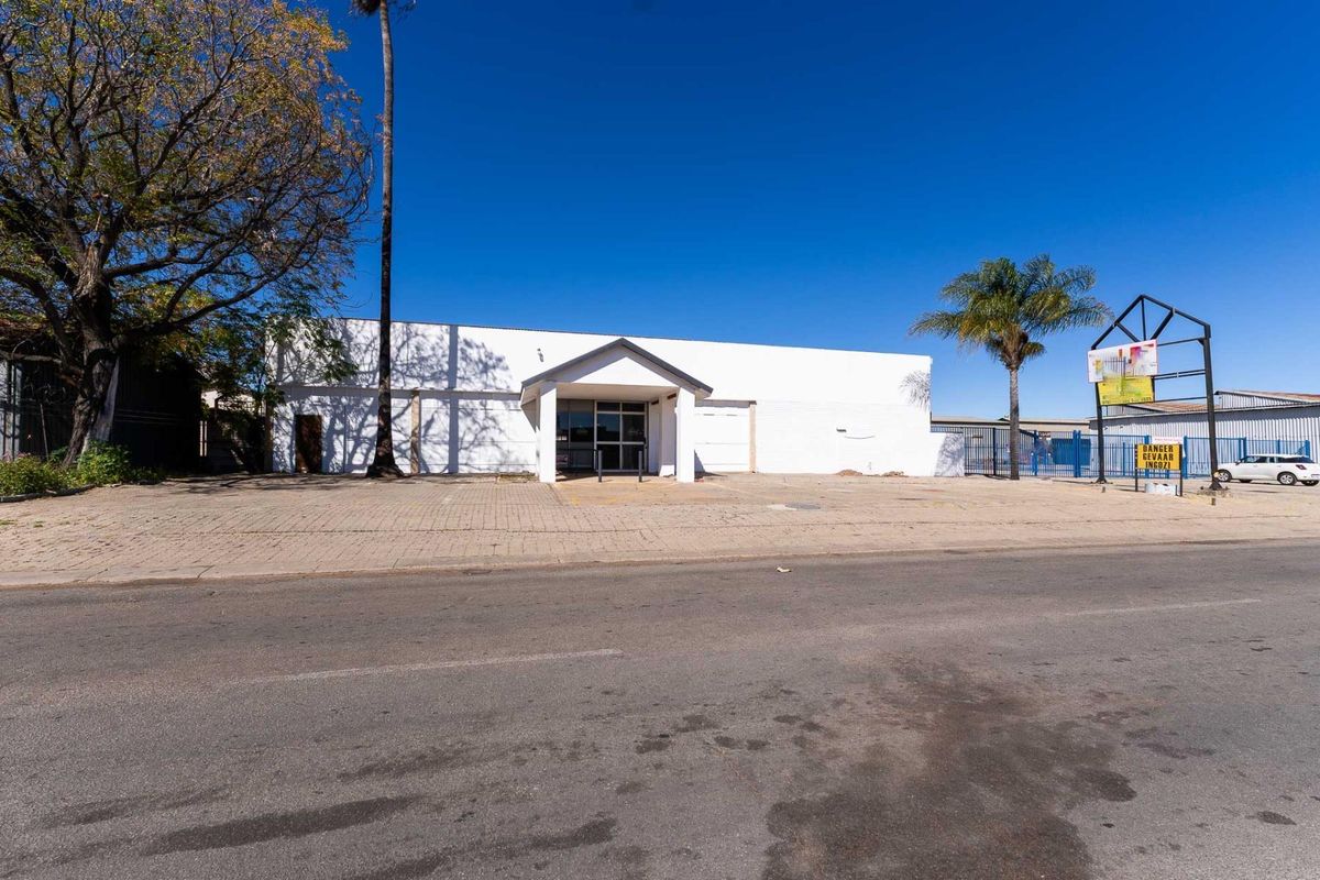 Front exterior view of an industrial property featuring a paved driveway, covered entrance, and perimeter fencing.