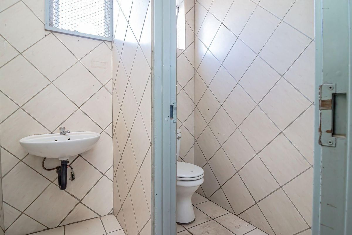 A functional industrial-style bathroom featuring a wall-mounted basin and a separate toilet cubicle with tiled walls and flooring.