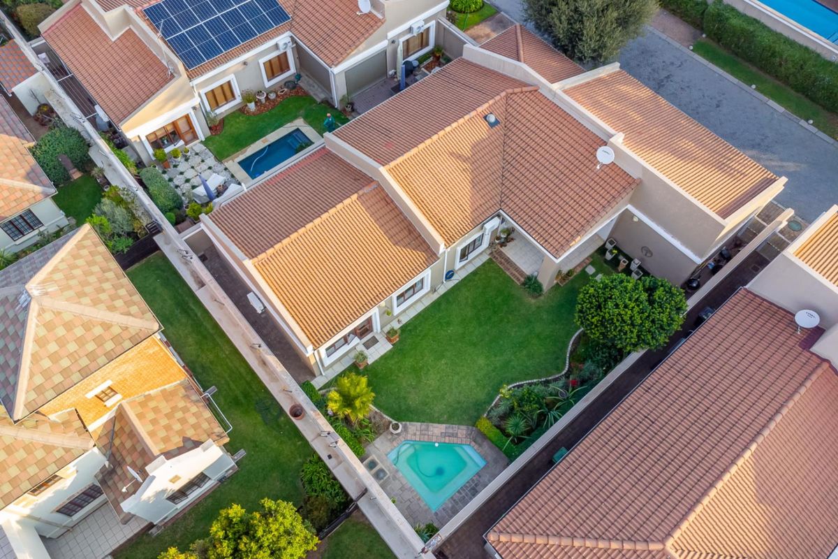 Aerial view of a townhouse property featuring a private garden, swimming pool, tiled roof, and installed solar panels.