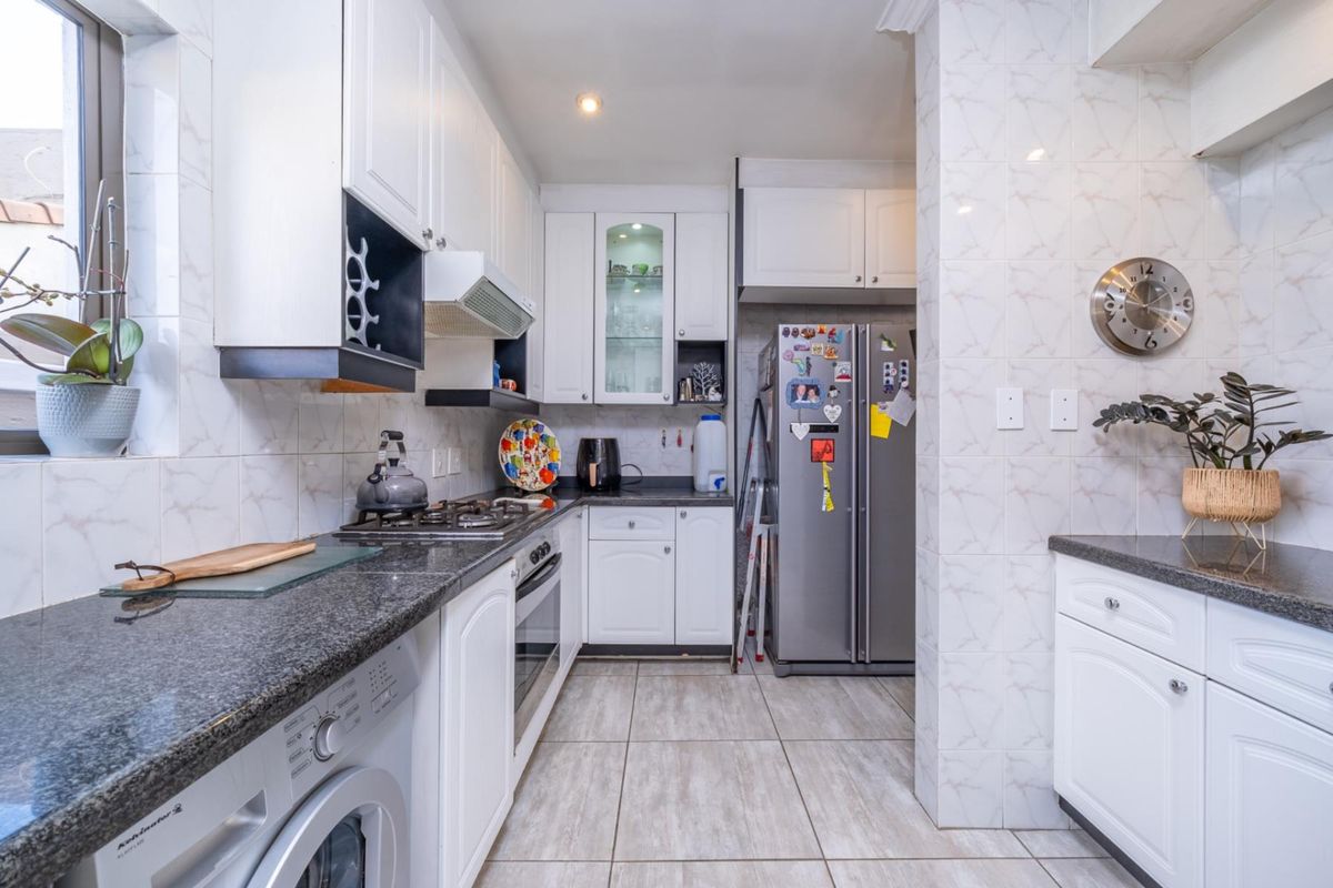 A functional kitchen featuring granite countertops, white cabinetry, a gas hob, built-in oven, and tiled finishes throughout.