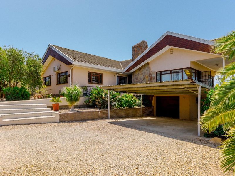 Front view of a residential house featuring a gravel driveway, attached carport, stone-clad chimney, and concrete steps leading to the entrance.