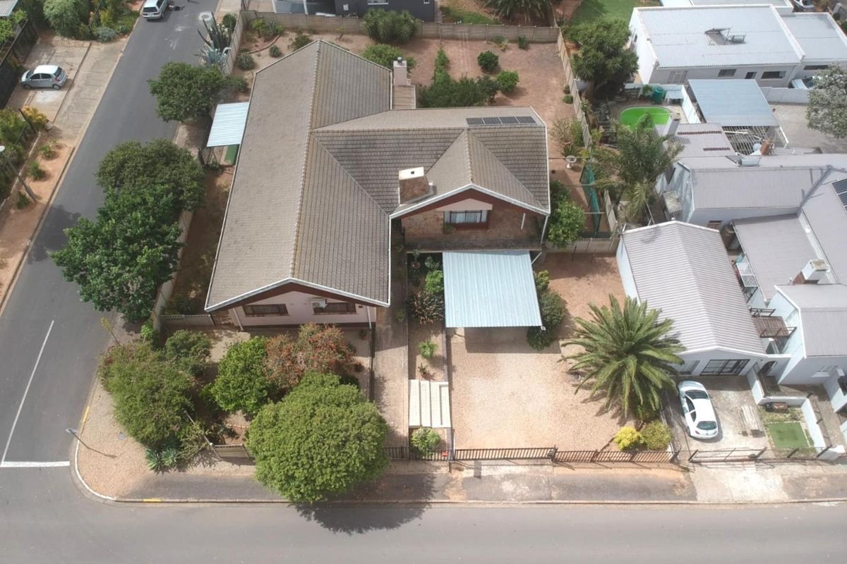 Aerial view of a residential property featuring a tiled roof, solar panels, a carport, and a spacious garden area.