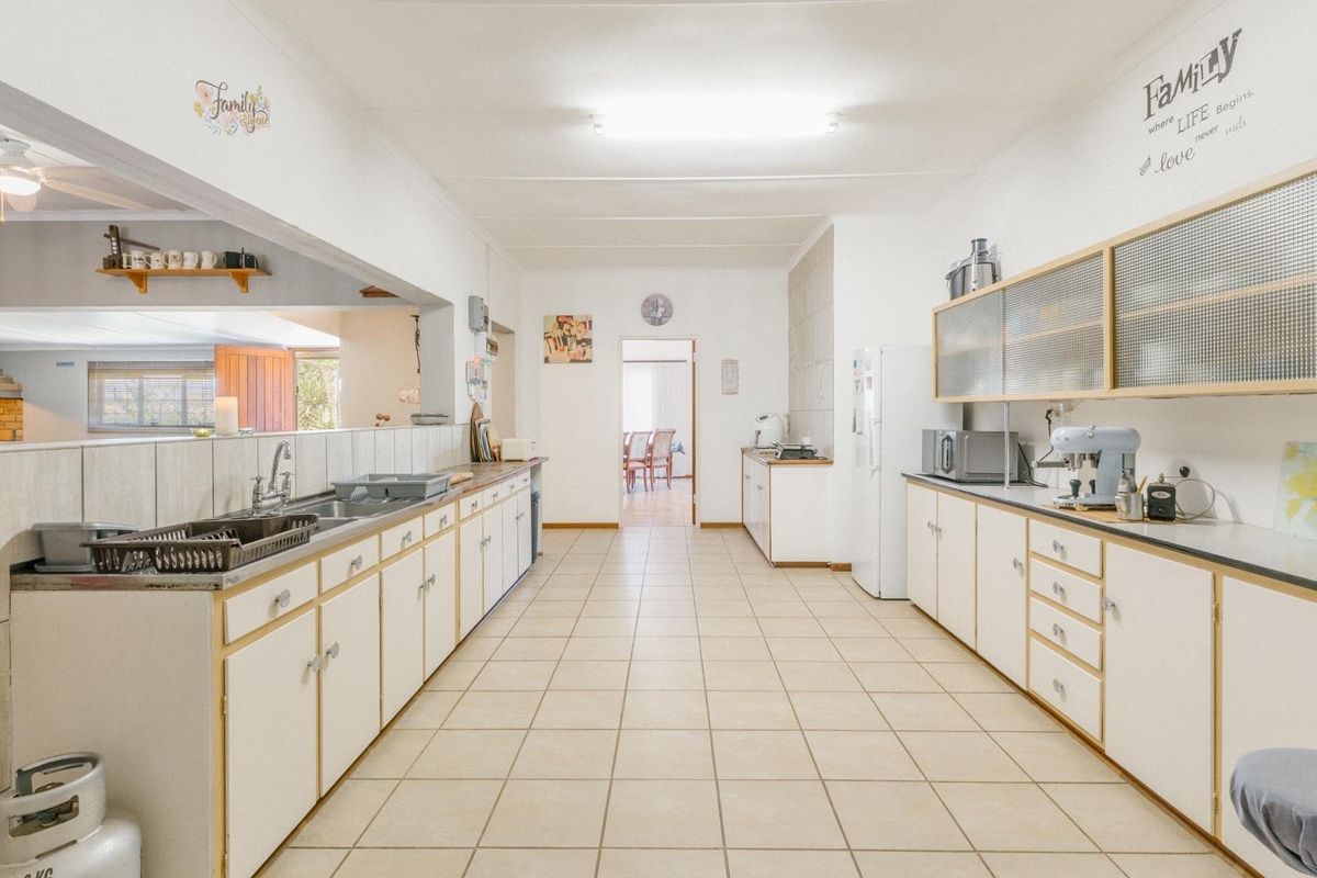 Spacious kitchen featuring extensive laminate cabinetry, tiled flooring, and a double sink, offering a functional layout with potential for modern updates.