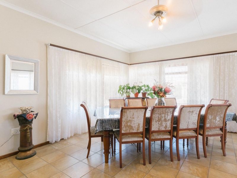 A bright dining room featuring tiled flooring, a ceiling fan, and large windows with curtain rails, providing a functional space for family meals.