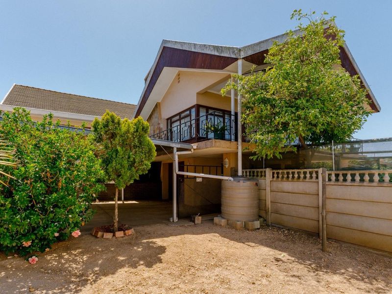 Rear view of the property featuring a multi-level structure, balcony with metal railing, concrete boundary wall, and a water storage tank.