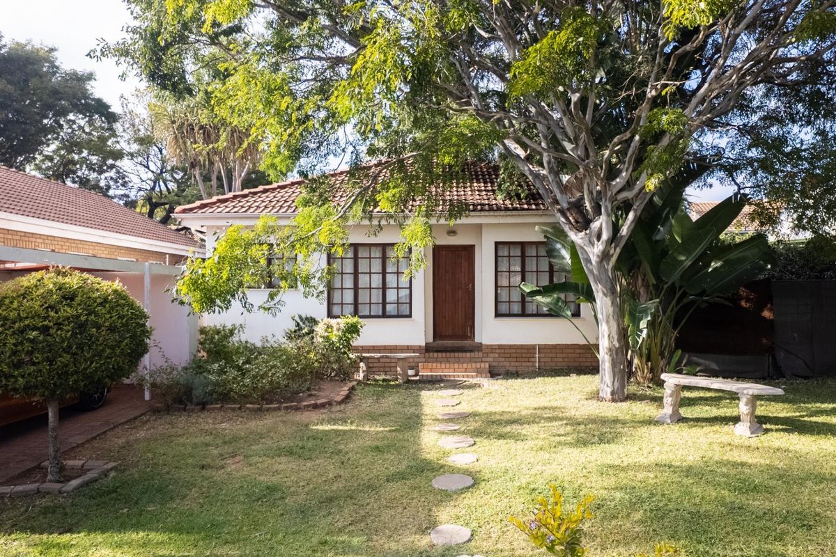 A view of the rear exterior of the house featuring a tiled roof, timber-framed windows, and a landscaped garden with a paved path.