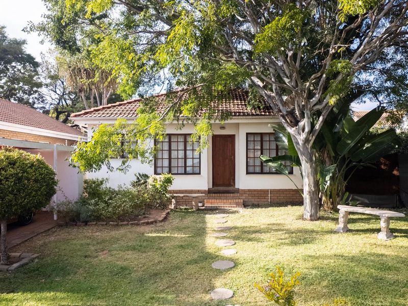 A view of the rear exterior of the house featuring a tiled roof, timber-framed windows, and a landscaped garden with a paved path.
