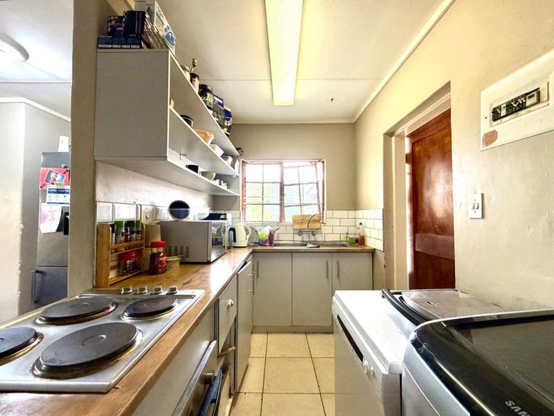 A functional kitchen featuring built-in cabinetry, an electric hob, tiled backsplash, and a stainless steel sink with natural light from the window.