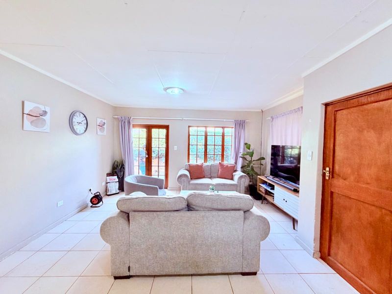 A bright living room featuring tiled flooring, timber-framed windows, and glass doors providing natural light and access to the exterior.