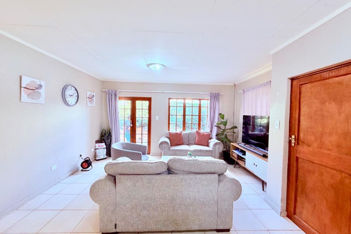 A bright living room featuring tiled flooring, timber-framed windows, and glass doors providing natural light and access to the exterior.