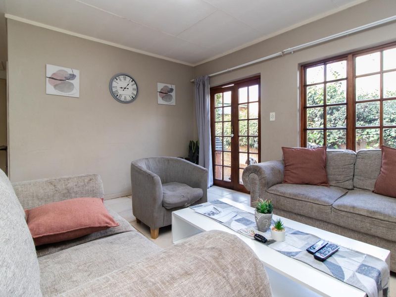 A comfortable living room featuring tiled flooring, timber-framed windows, and glass doors providing direct access to the outdoor area.