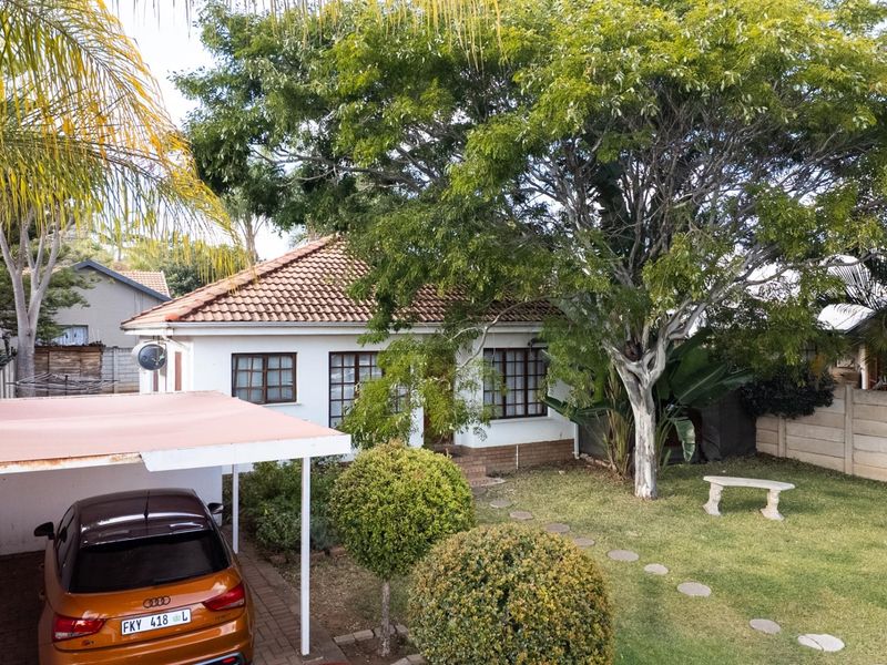 Front view of a single-story house featuring a tiled roof, timber-framed windows, a carport, and a landscaped front garden with a paved walkway.