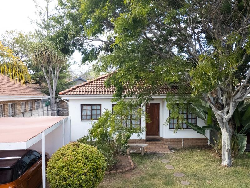 Front elevation of a single-story house featuring a tiled roof, brick accents, timber-framed windows, and an attached carport with a landscaped front garden.