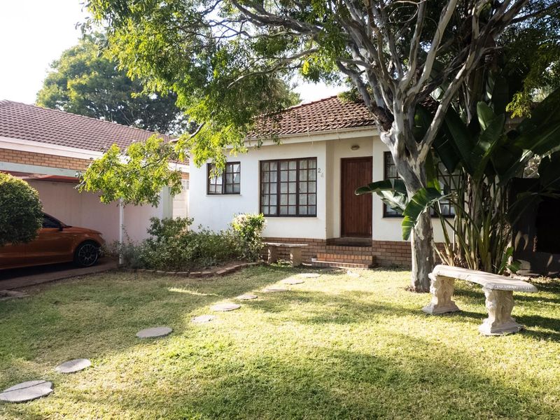 Front view of a charming single-story house featuring a tiled roof, timber-framed windows, and an attached carport, set within a landscaped garden.