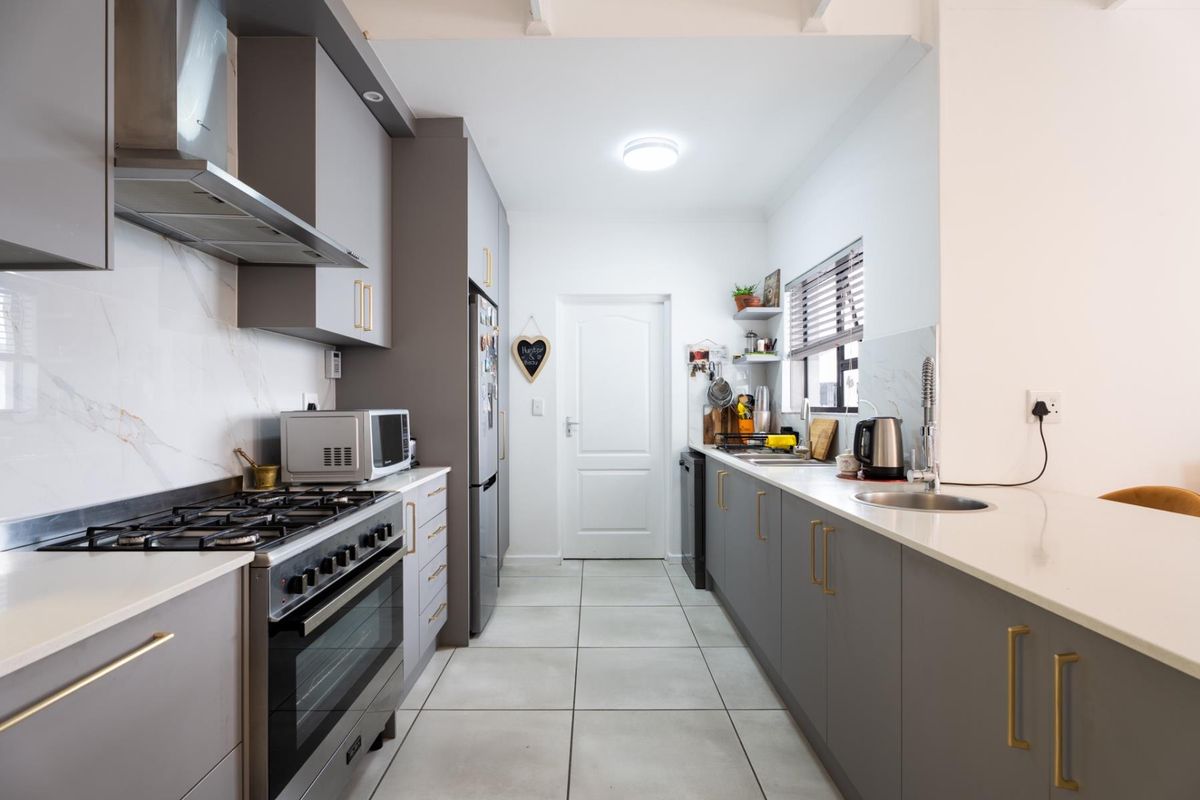 Modern galley-style kitchen featuring grey cabinetry, quartz countertops, a gas stove with extractor fan, and tiled flooring.