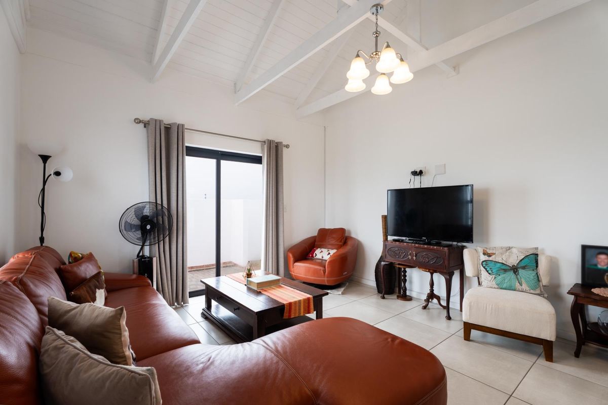 A bright living room featuring a vaulted ceiling with exposed rafters, tiled flooring, and a sliding glass door providing access to the outdoor area.