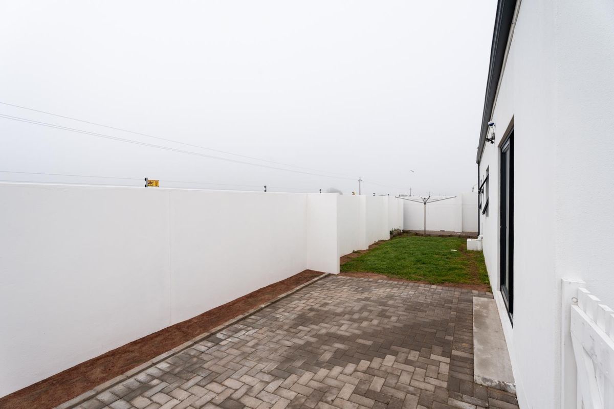 A private rear garden featuring a paved patio area, a small lawn, and high boundary walls for added privacy.