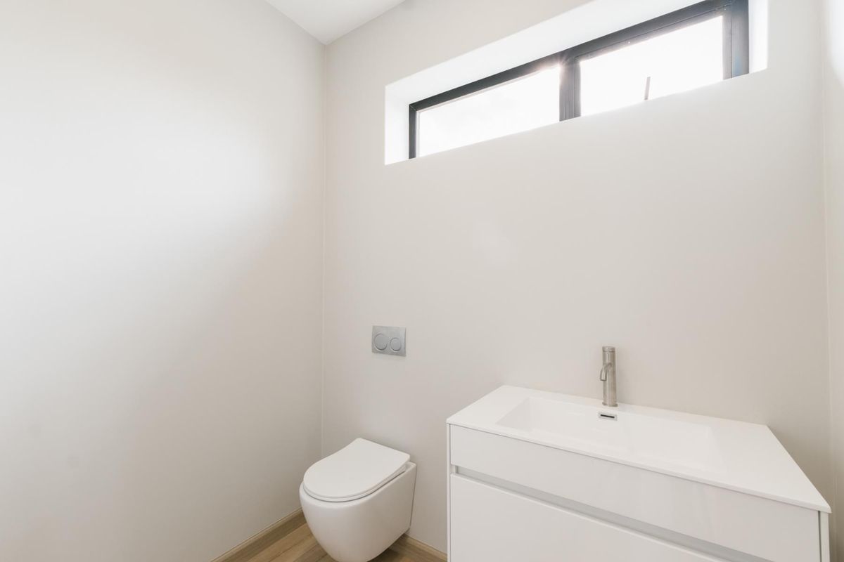 A modern, minimalist powder room featuring a wall-mounted toilet with a concealed cistern and a sleek white vanity with a basin.