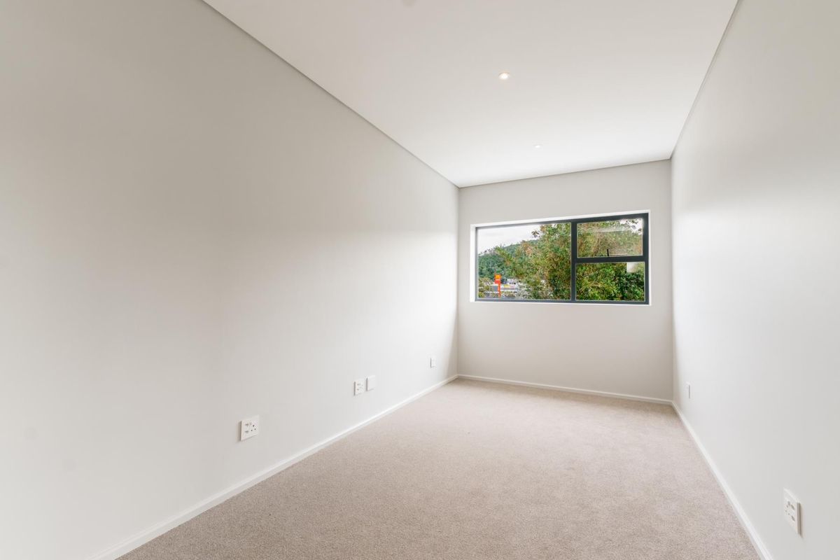 A bright, neutral, and empty bedroom featuring clean finishes, recessed ceiling lighting, and a large window with a view.