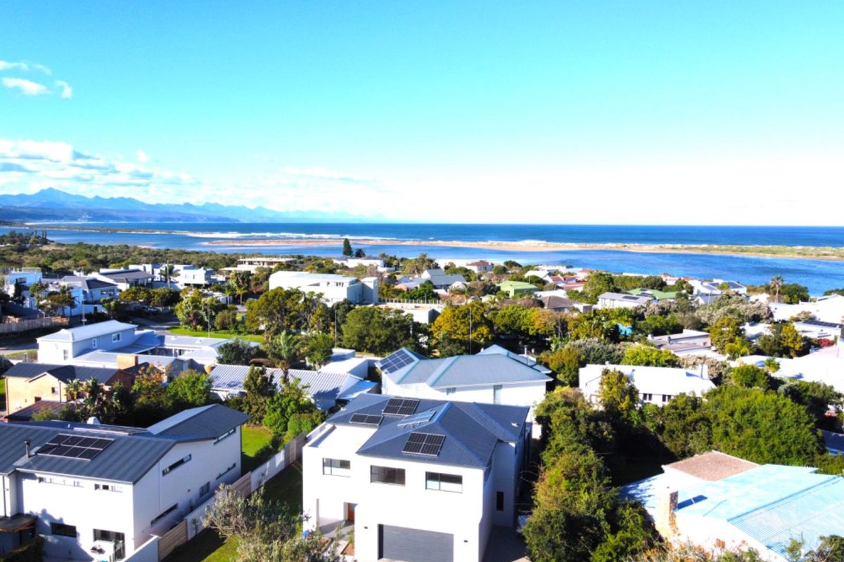 An elevated aerial view of a coastal residential neighborhood featuring modern homes with solar panels, overlooking a scenic estuary and the ocean.