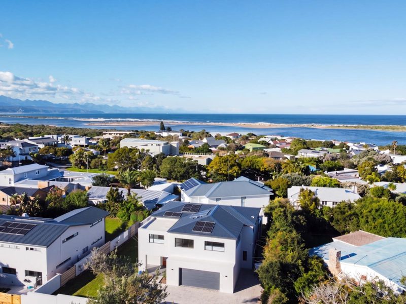 Aerial view of a modern residential property featuring a metal roof with solar panels, a paved driveway, and proximity to the coastline.