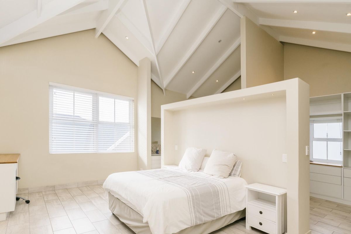 Spacious bedroom featuring a high vaulted ceiling with exposed beams, tiled flooring, and a central partition wall creating a dedicated sleeping area.