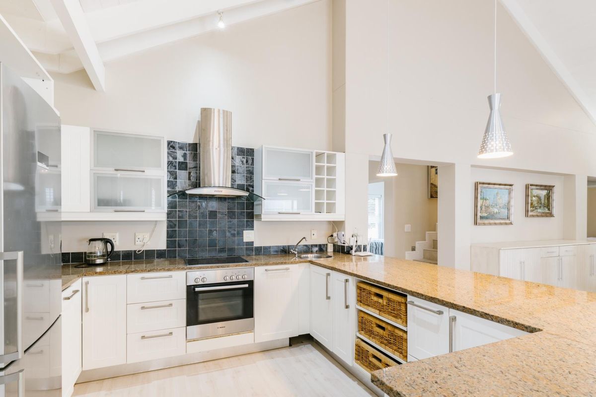 Modern open-plan kitchen featuring granite countertops, white cabinetry, stainless steel oven, extractor fan, and a vaulted ceiling with pendant lighting.