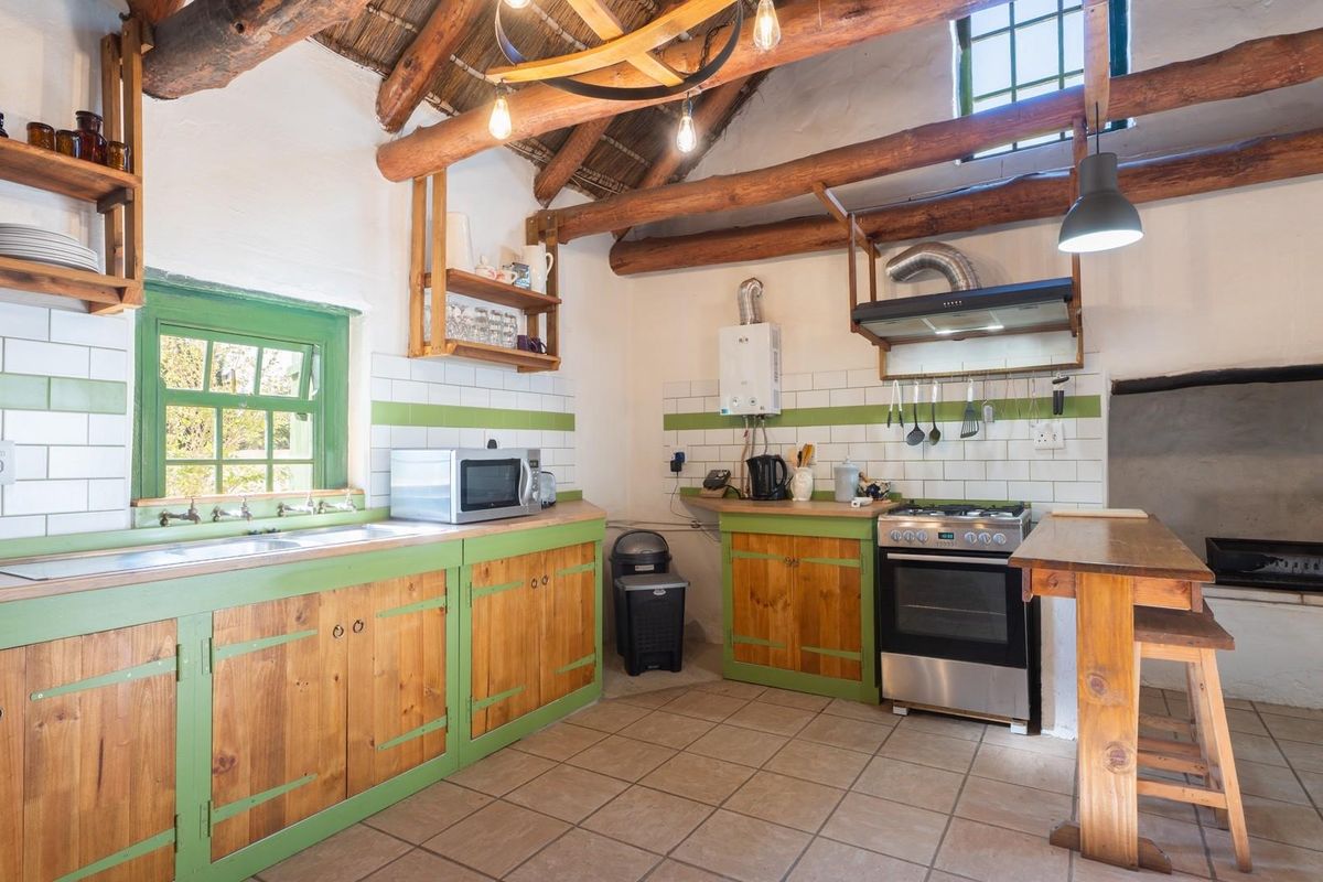 Rustic kitchen featuring exposed timber ceiling beams, wooden cabinetry with green accents, tiled backsplash, and a built-in fireplace area.