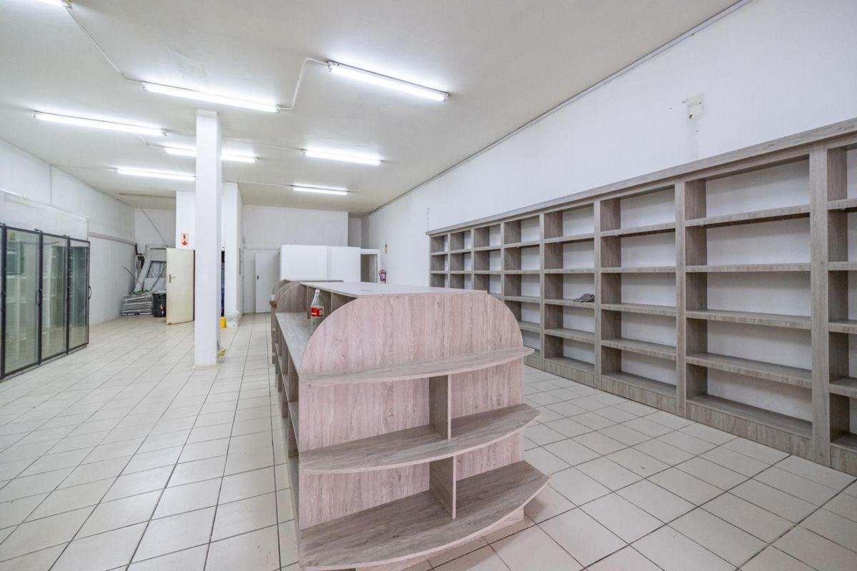 Spacious retail interior featuring built-in wooden shelving units, tiled flooring, and integrated fluorescent lighting, suitable for a variety of commercial business applications.