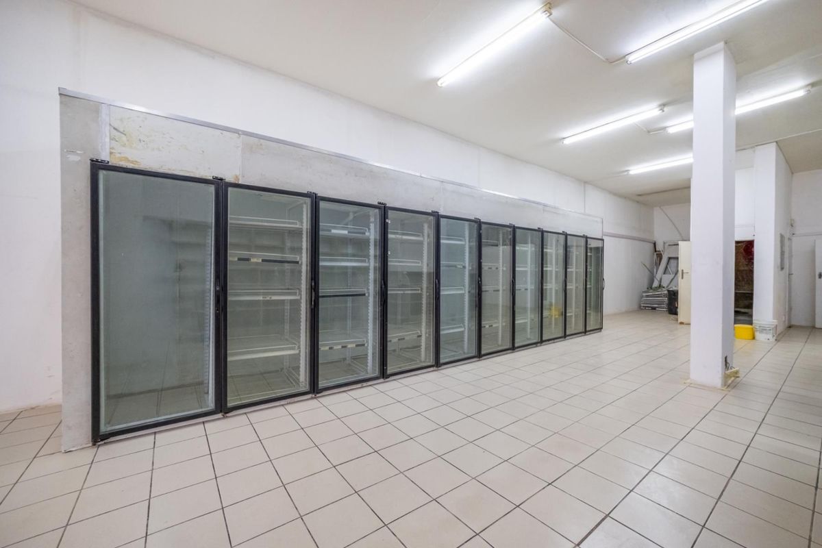 Retail space featuring a long bank of built-in glass-front commercial refrigeration units, tiled flooring, and fluorescent overhead lighting.