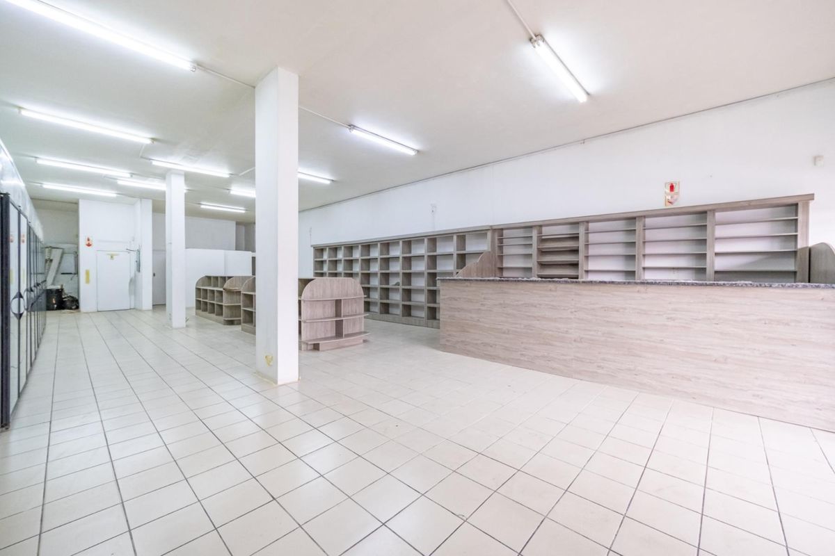 Spacious retail floor area featuring tiled flooring, built-in wooden shelving units, a service counter, and overhead fluorescent lighting.