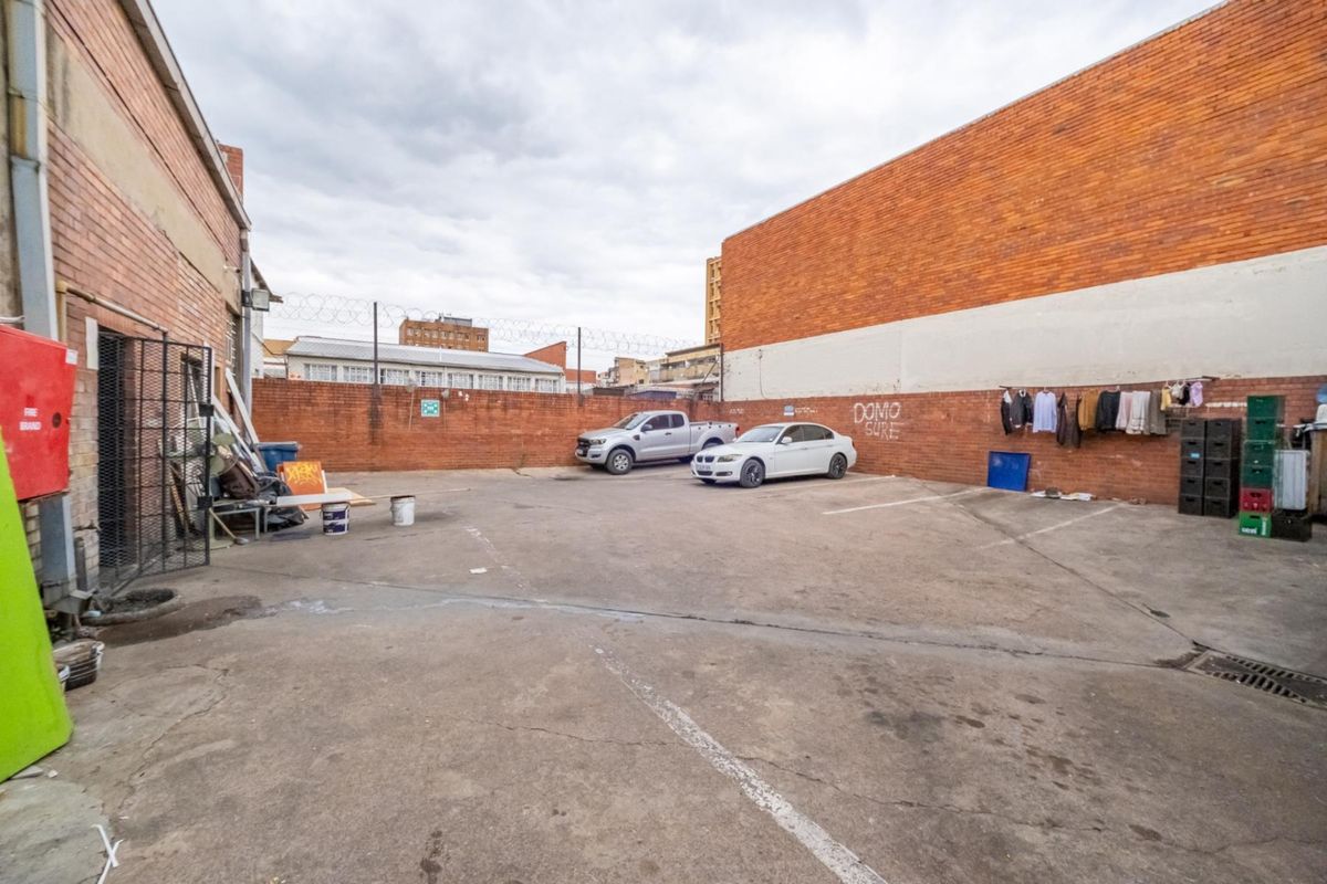 An open-air paved rear yard area featuring perimeter brick walls with security fencing, suitable for parking or utility access.