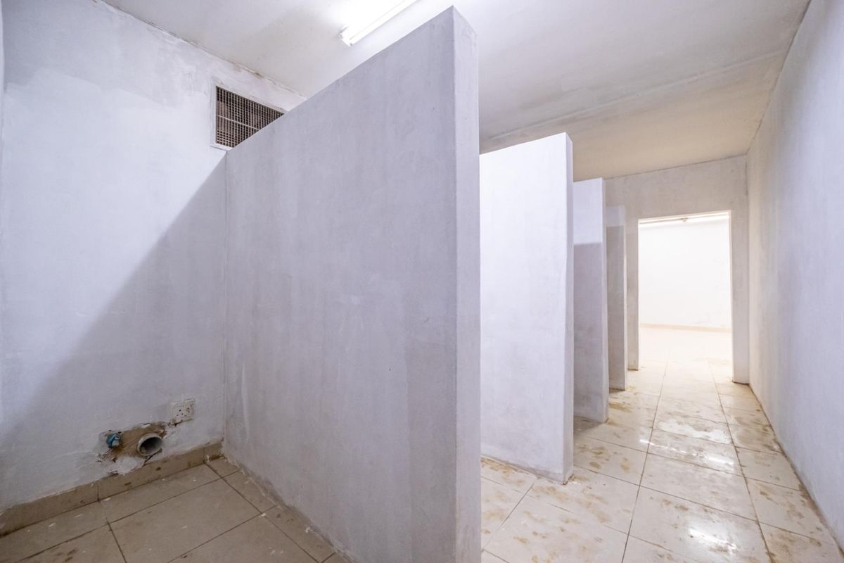 A utilitarian space featuring multiple partitioned cubicle walls, tiled flooring, and exposed plumbing connections, suitable for renovation or conversion into a functional restroom facility.
