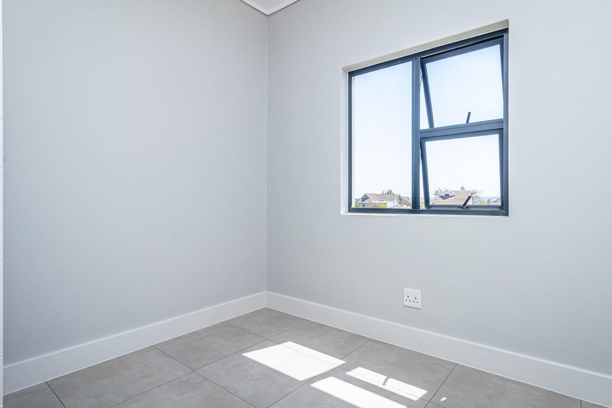A bright, empty bedroom featuring neutral grey walls, modern tiled flooring, and a dark-framed window providing natural light.