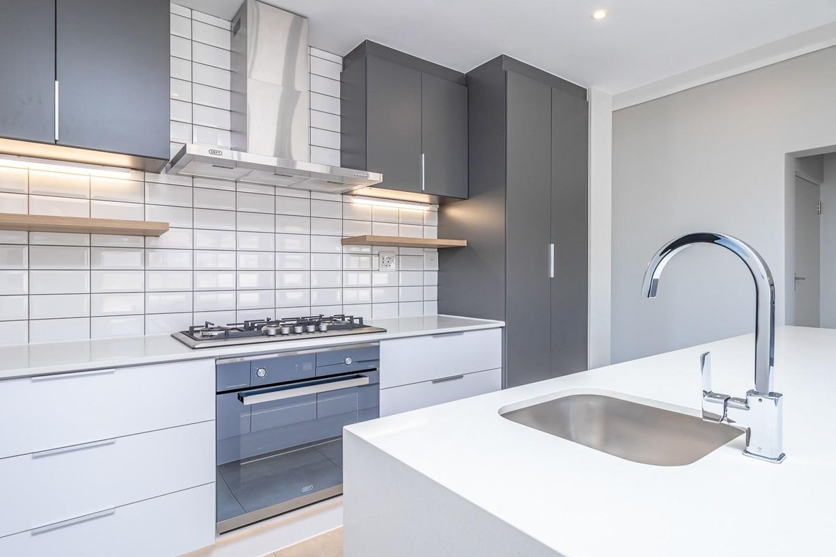Modern kitchen featuring sleek white and grey cabinetry, stone countertops, a gas hob, stainless steel extractor fan, and a central island with a sink.
