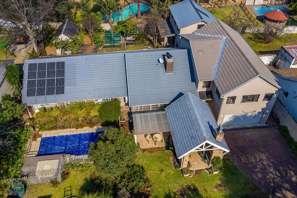 Aerial view of a residential property featuring a tiled roof, solar panels, a swimming pool with cover, and a covered patio area.