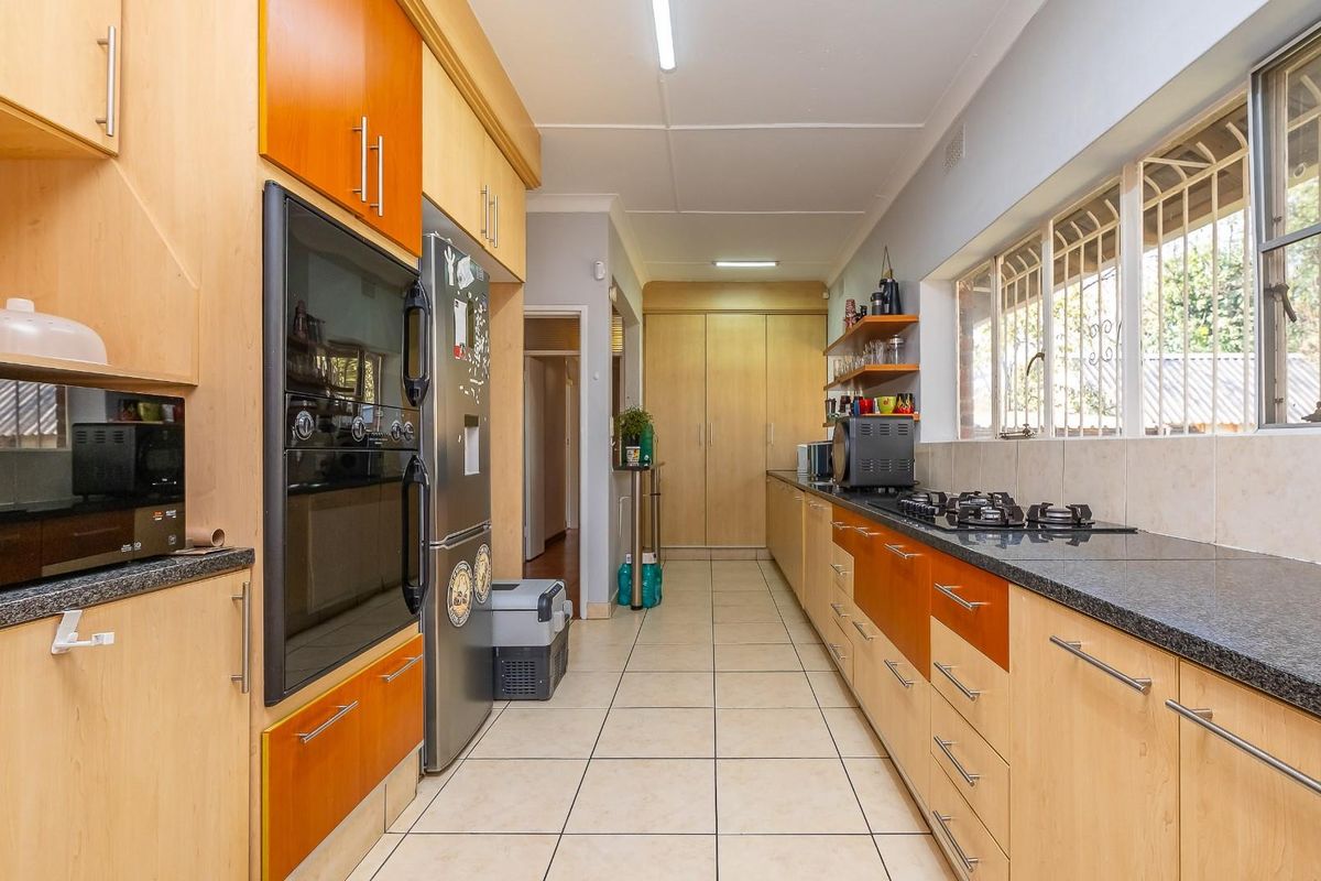 A functional galley-style kitchen featuring light wood cabinetry, dark granite countertops, a built-in oven, and a gas hob with tiled splashbacks.