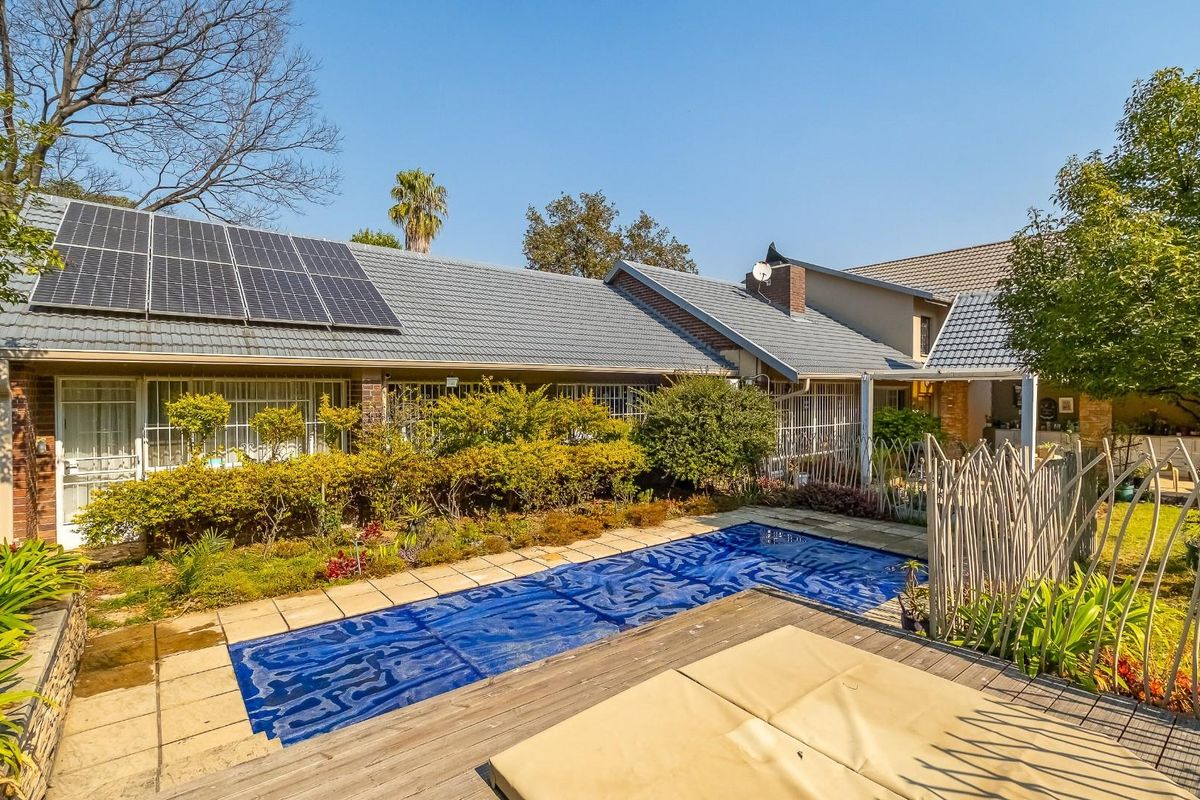 Rear view of the property featuring a swimming pool with a cover, landscaped garden, and solar panels installed on the tiled roof.